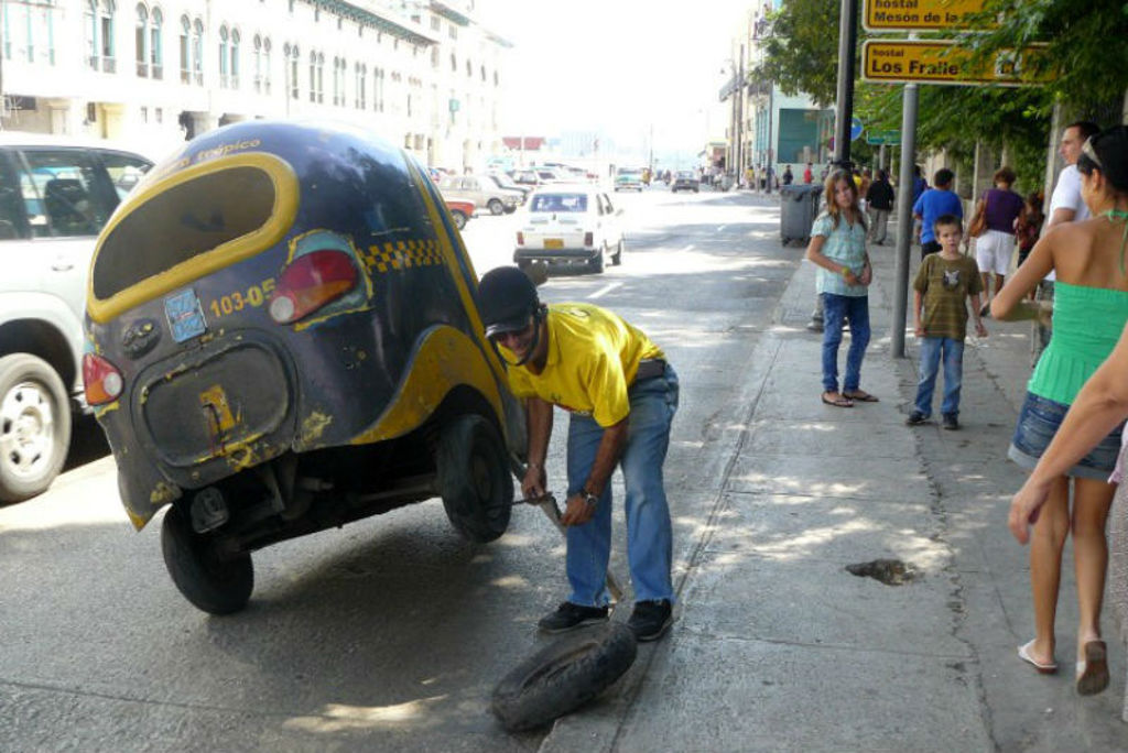 Monteur verwisselt band van een cocotaxi op straat in Cuba.