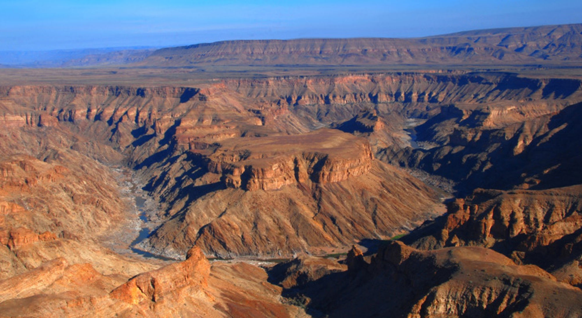 Fish River Canyon Namibië Panoramisch uitzicht over een diepe canyon met rotsformaties en een droge rivierbedding onder een heldere blauwe lucht.