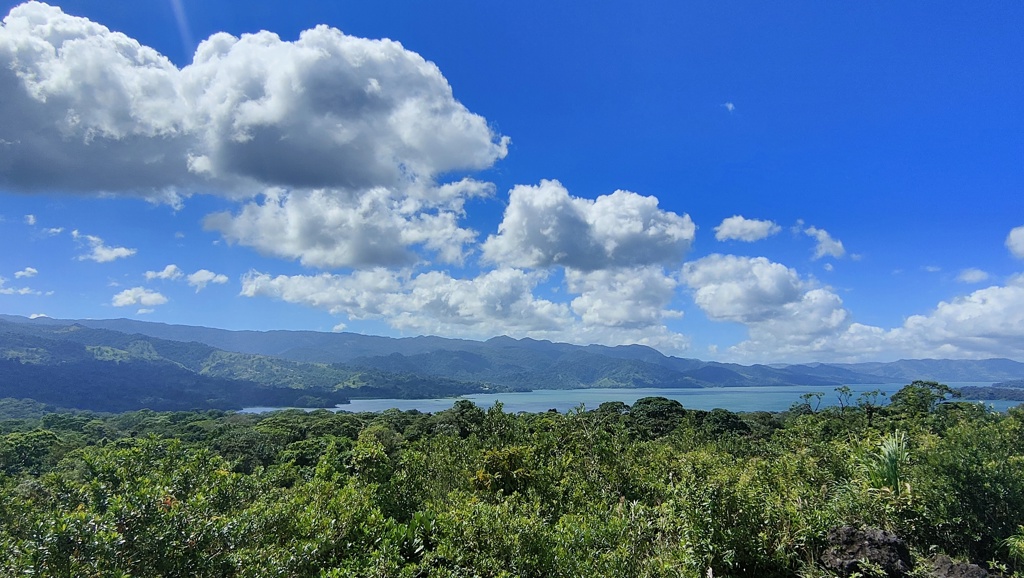 Uitzicht over het regenwoud en een meer in Costa Rica, met bergen onder een blauwe lucht met wolken.