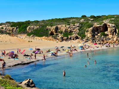 Zandstrand met zwemmers en parasols bij rotsachtige kust op Sicilië, tijdens de 20-daagse reis Amalfikust en Sicilië.