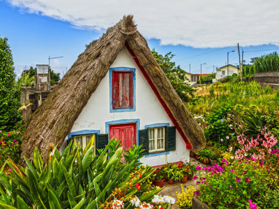 Traditioneel Santana-huis met rieten dak en kleurrijke luiken, omringd door bloemen op Madeira.