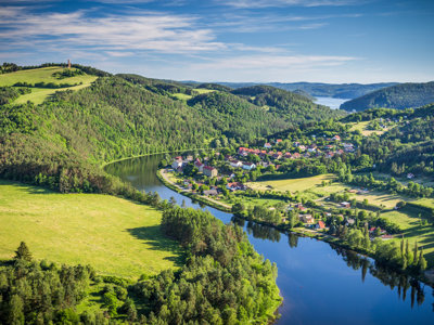 Uitzicht op de rivier de Moldau met dorp en groene heuvels, op de fietsroute van Praag naar Wenen.