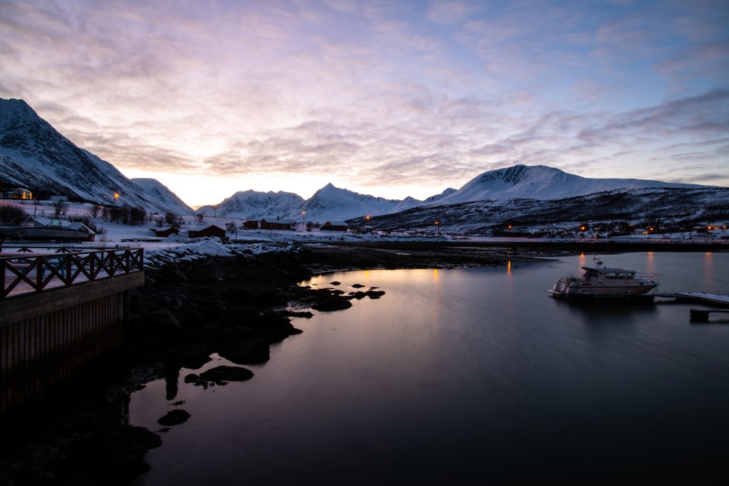 Sneeuwbergen en fjord bij schemering in Noorwegen, met boot aan de steiger.
