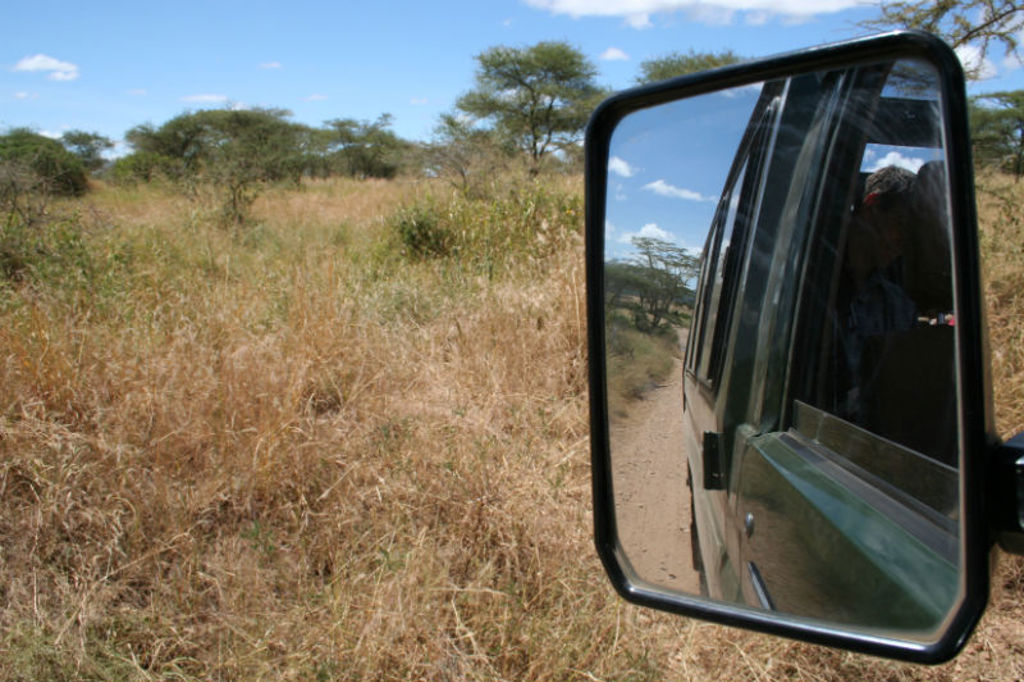 Safari-jeep op zandpad door de savanne in Kenia, gezien via de zijspiegel.