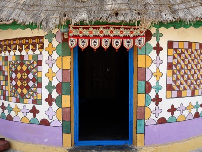 Kleurrijk beschilderde gevel met blauwe deuropening en rieten dak in Gujarat tijdens de 19-daagse route.