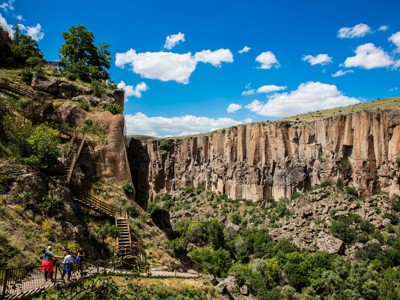 Wandelaars op trappenpad in de Ihlara-vallei, Cappadocië, langs steile rotswanden onder blauwe lucht.