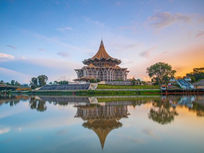 Het Sarawak State Legislative Assembly-gebouw in Kuching weerspiegeld in het water bij zonsondergang.