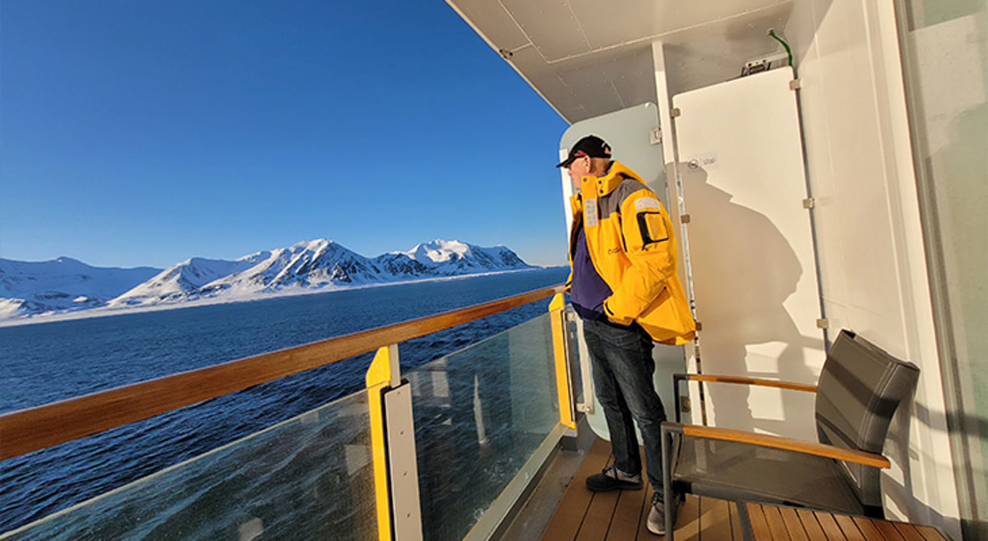 Balkon Ultramarine Man op het dek van een cruiseschip met uitzicht op besneeuwde bergen en zee.