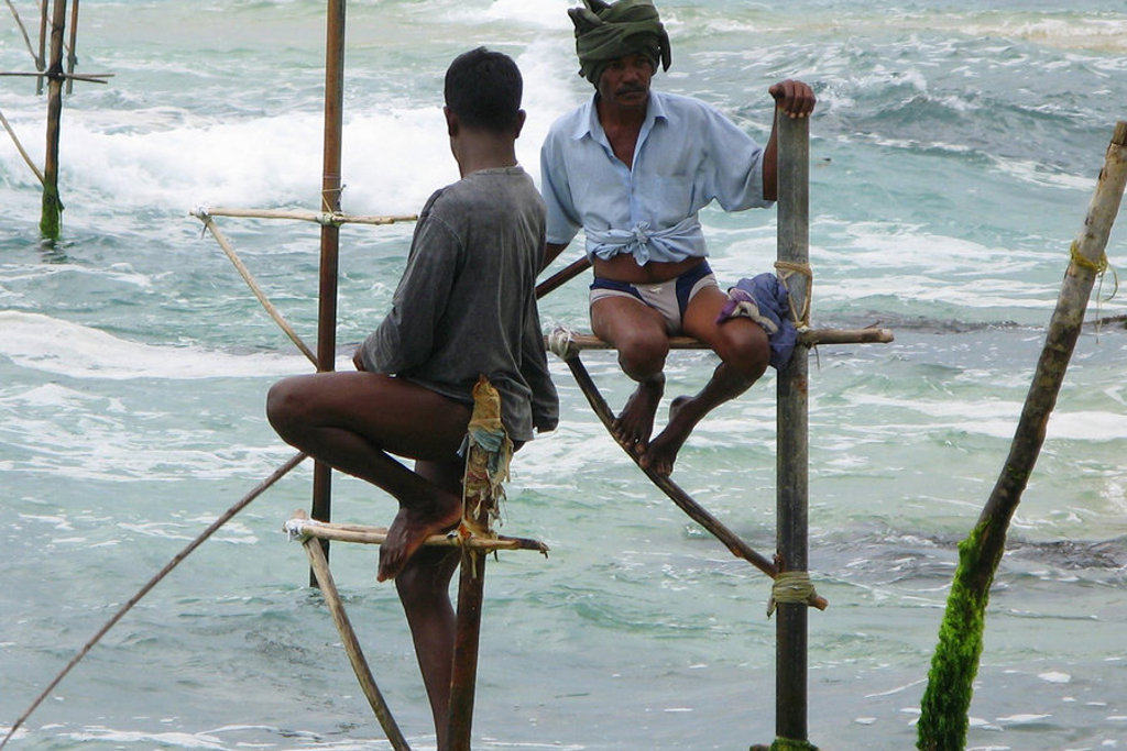 Steltvissers aan de kust van Sri Lanka, zittend op houten stokken boven de golven.
