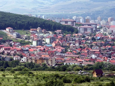 Uitzicht over een stad in Roemenië met rode daken, flats en groene heuvels op de achtergrond.