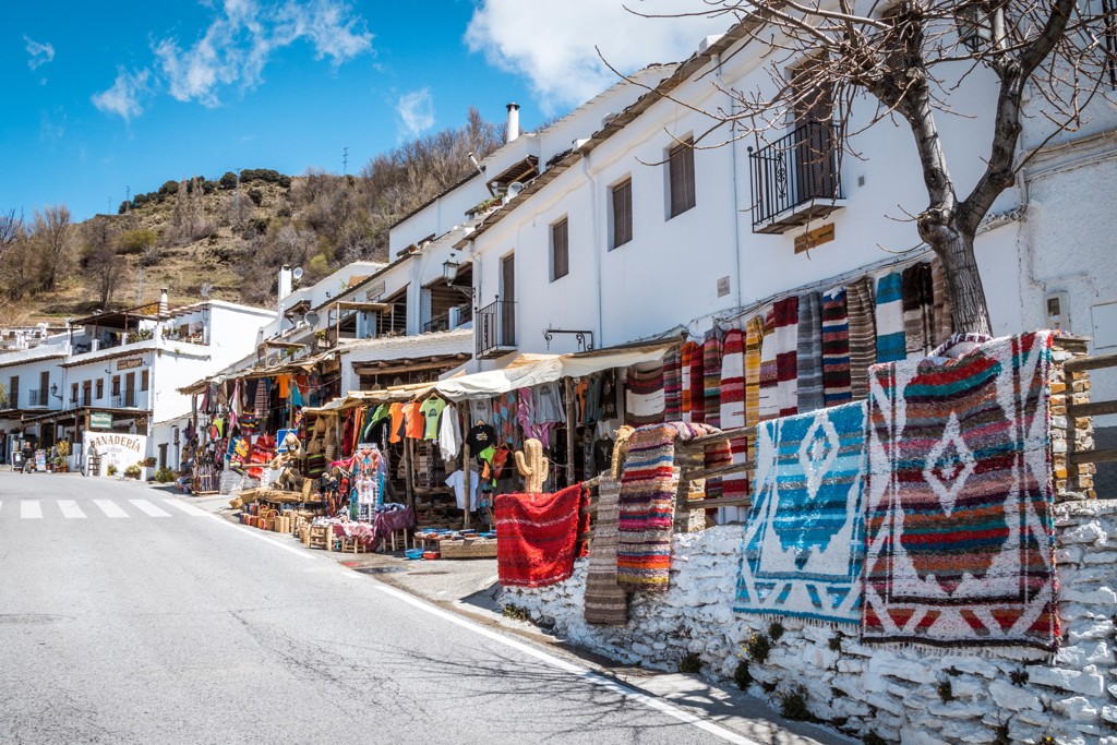 Straat in een wit dorp in de Sierra Nevada bij Granada met kleurrijke tapijten en souvenirs aan kraampjes.