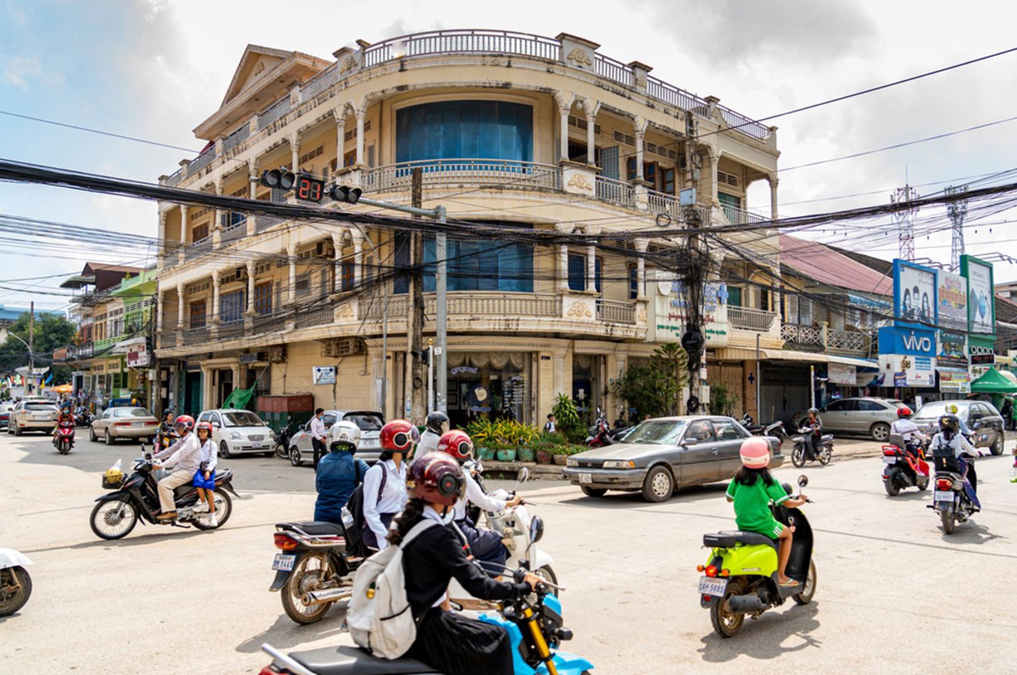 Straatbeeld in Phnom Penh, Cambodja, met druk verkeer en een historisch gebouw op de hoek.