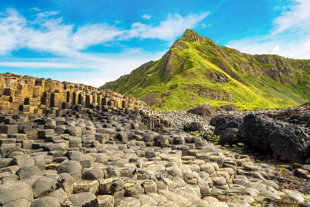 Basaltzuilen van de Giant’s Causeway aan de kust van Noord-Ierland, met groene heuvels op de achtergrond.