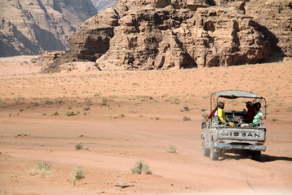 Jeep met reizigers in de Wadi Rum-woestijn in Jordanië, met rotsformaties op de achtergrond.