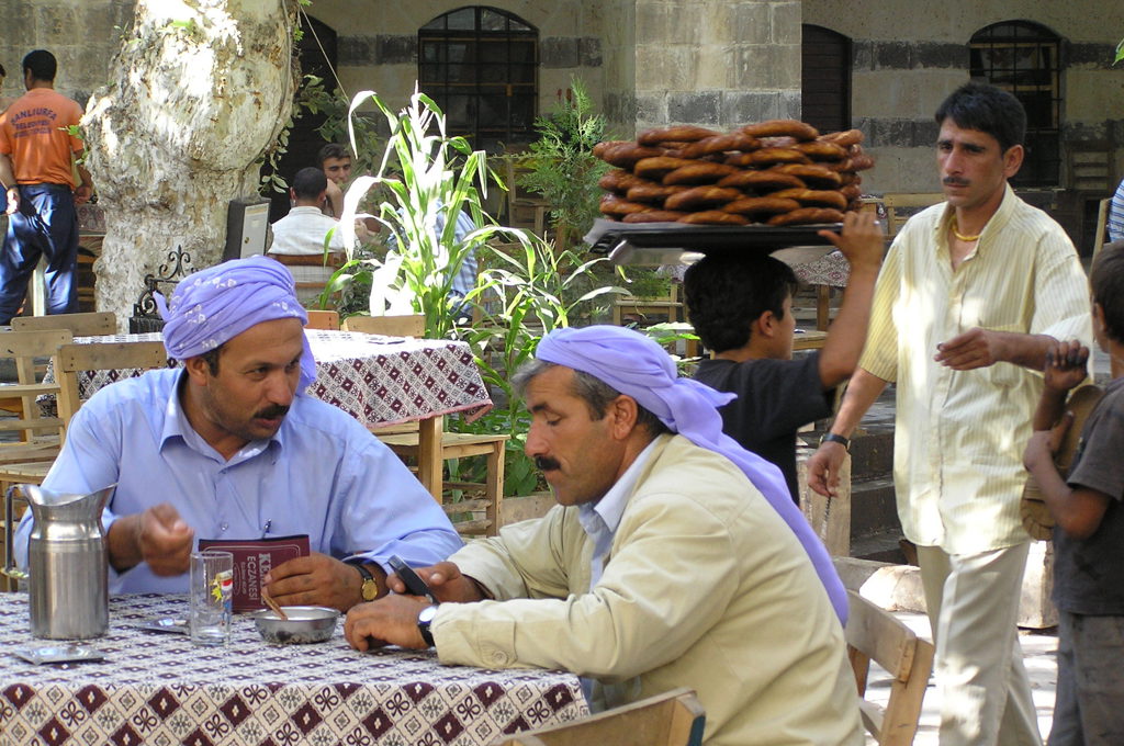 Lokale mannen in een theetuin met traditionele kleding en een verkoper met brood, tijdens een familiereis Turkije.