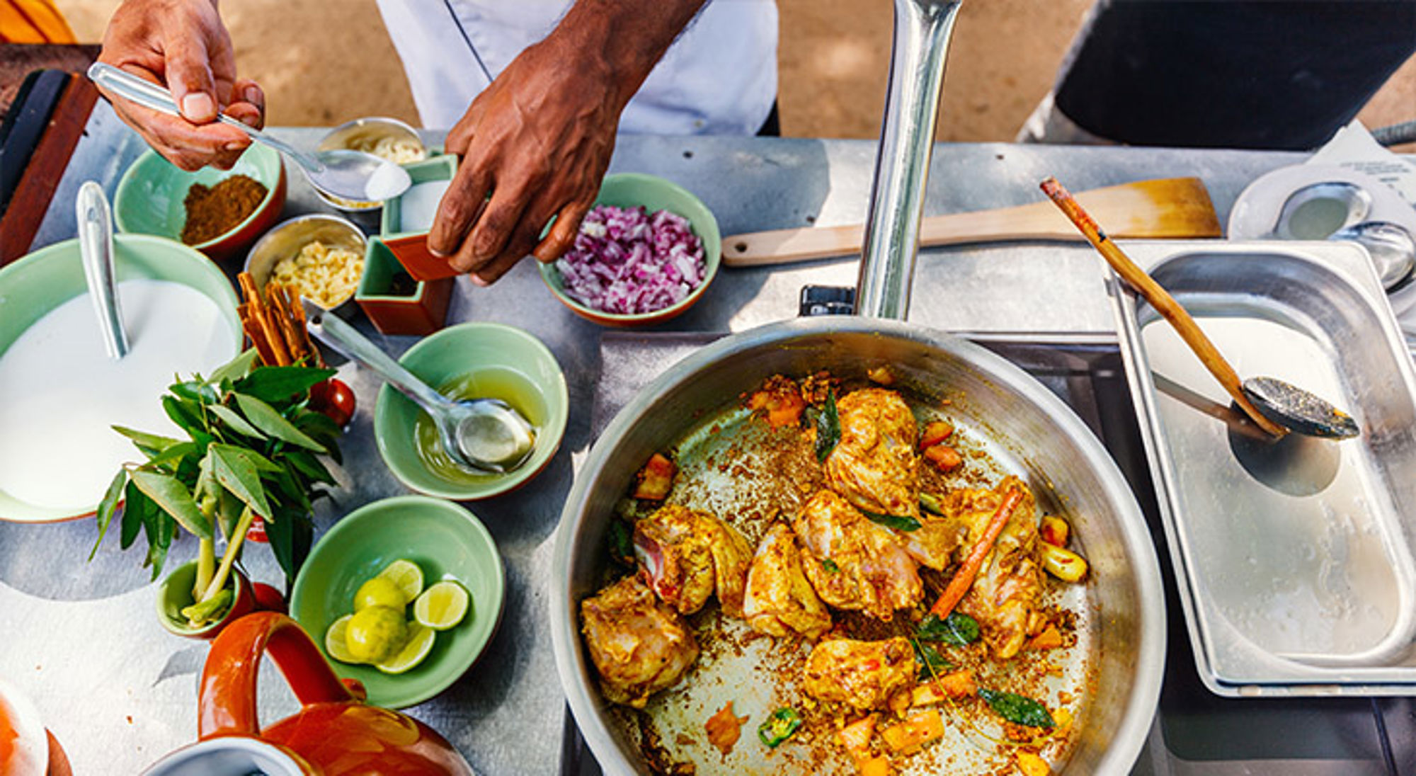 Kookworkshop Sri Lanka Kok bereidt kruidige kip in een pan met verse ingrediënten op een werkblad.
