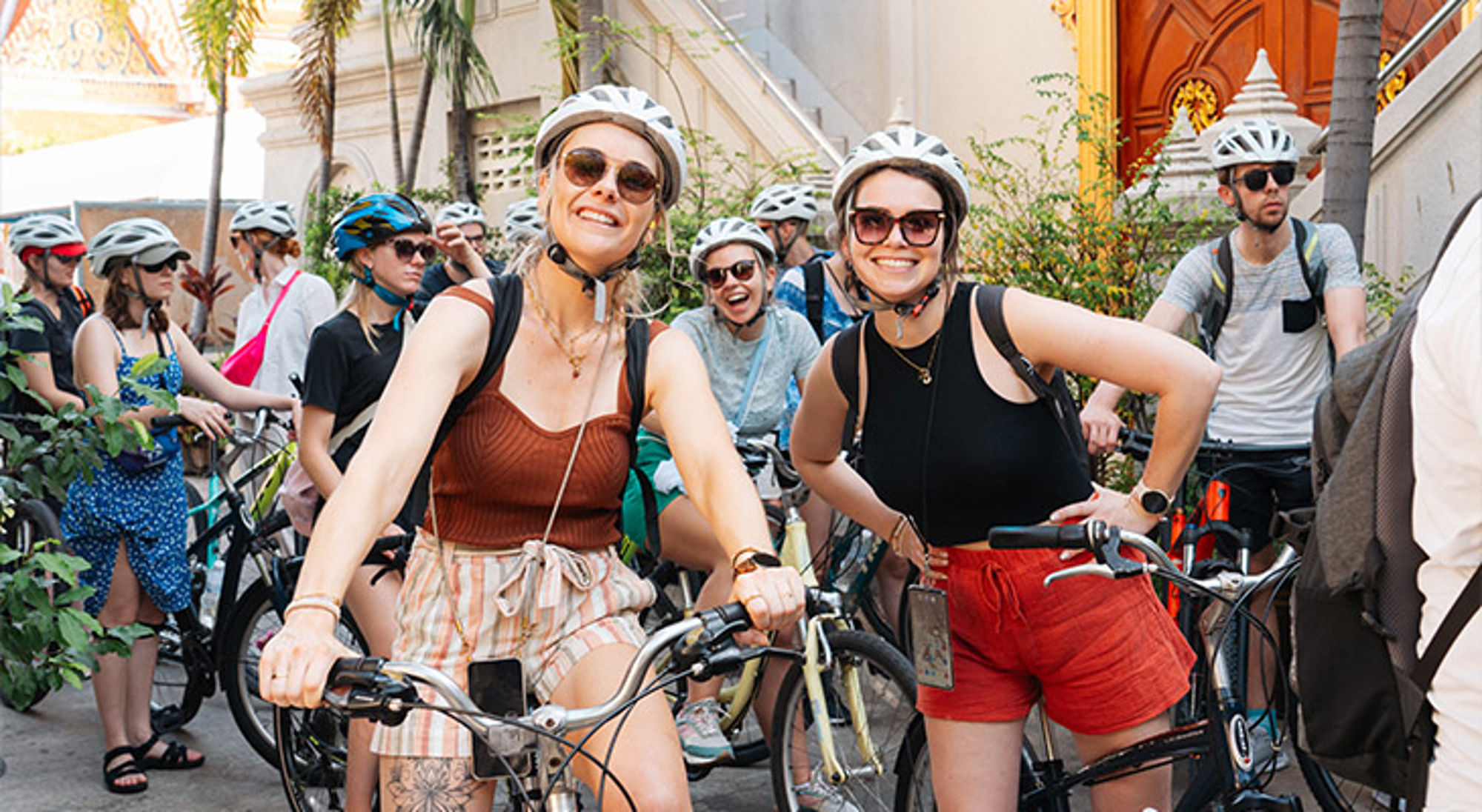 Groep fietsers met helm en zonnebril tijdens een stadstour, met tempel op de achtergrond.