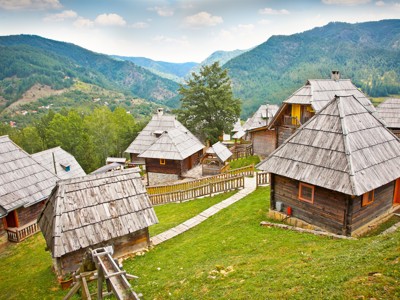 Houten bergdorp met traditionele huisjes en groene heuvels langs de Route Balkan rondreis.