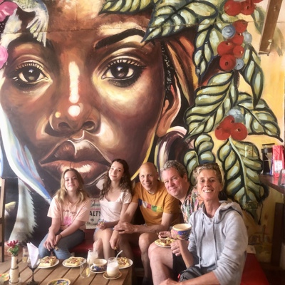 Familie geniet van koffie en taart in Colombiaans café met kleurrijke muurschildering op de achtergrond.