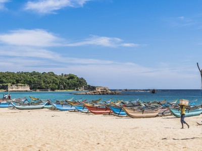 Kleurrijke vissersboten op het strand aan de kust van Sri Lanka, met helderblauwe zee en groene heuvels.