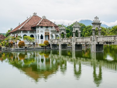 Taman Ujung Water Palace op Bali met sierbrug en vijver voor een wit paleis, met bergen op de achtergrond.