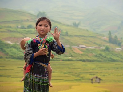 Meisje in traditionele kleding met baby op de rug, voor rijstterrassen in Vietnam tijdens route China & Vietnam, 20 dagen.