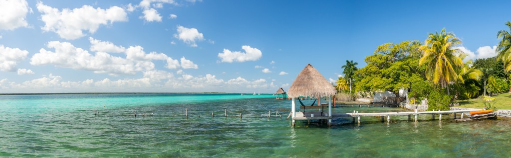 Tropisch strand in Mexico met turquoise water, palmbomen en rieten strandhut op een pier.