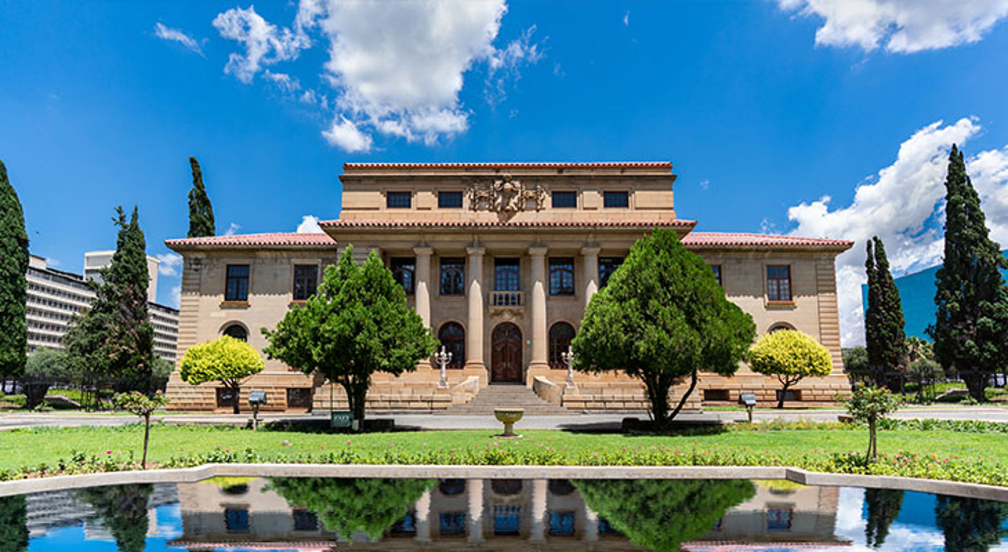Hooggerechtshof in Bloemfontein Union Buildings in Pretoria, Zuid-Afrika, met reflectievijver en tuinen onder een blauwe lucht.