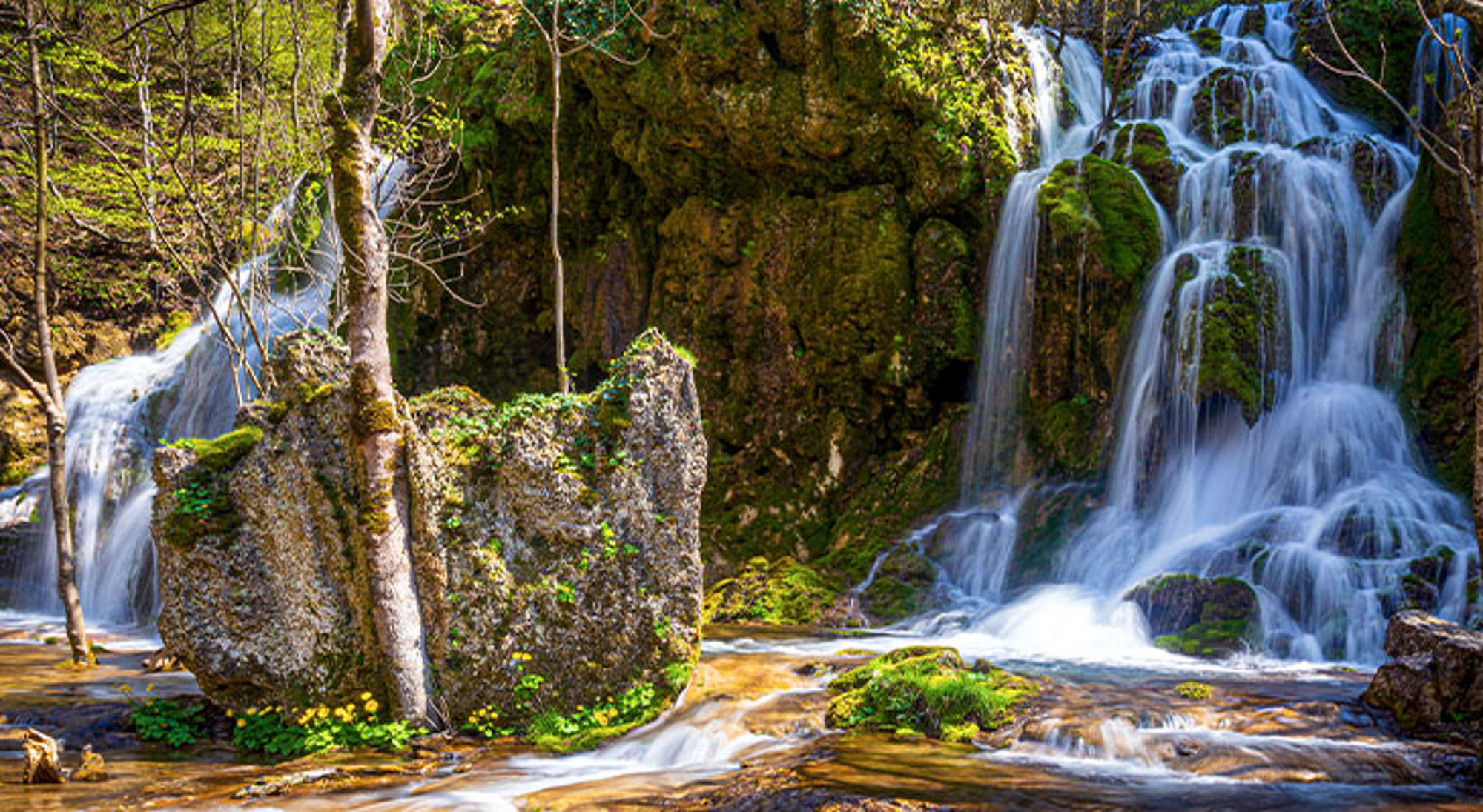 Bigar waterfall Waterval stroomt over met mos begroeide rotsen in een groen bos.