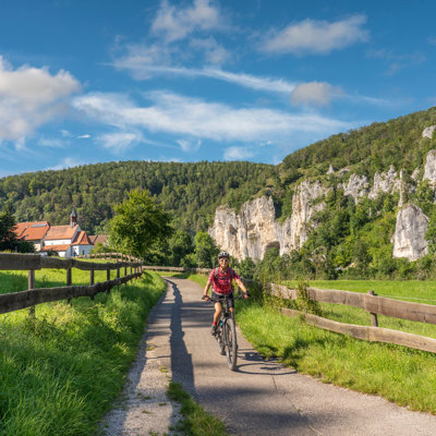 Fietser op het Donauradweg-fietspad langs groene weiden en rotswanden tijdens een fietsvakantie langs de Donau.