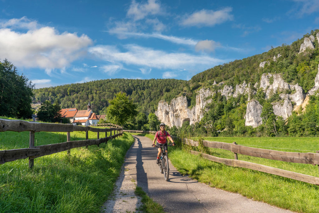 Fietser op het Donauradweg-fietspad langs groene weiden en rotswanden tijdens een fietsvakantie langs de Donau.