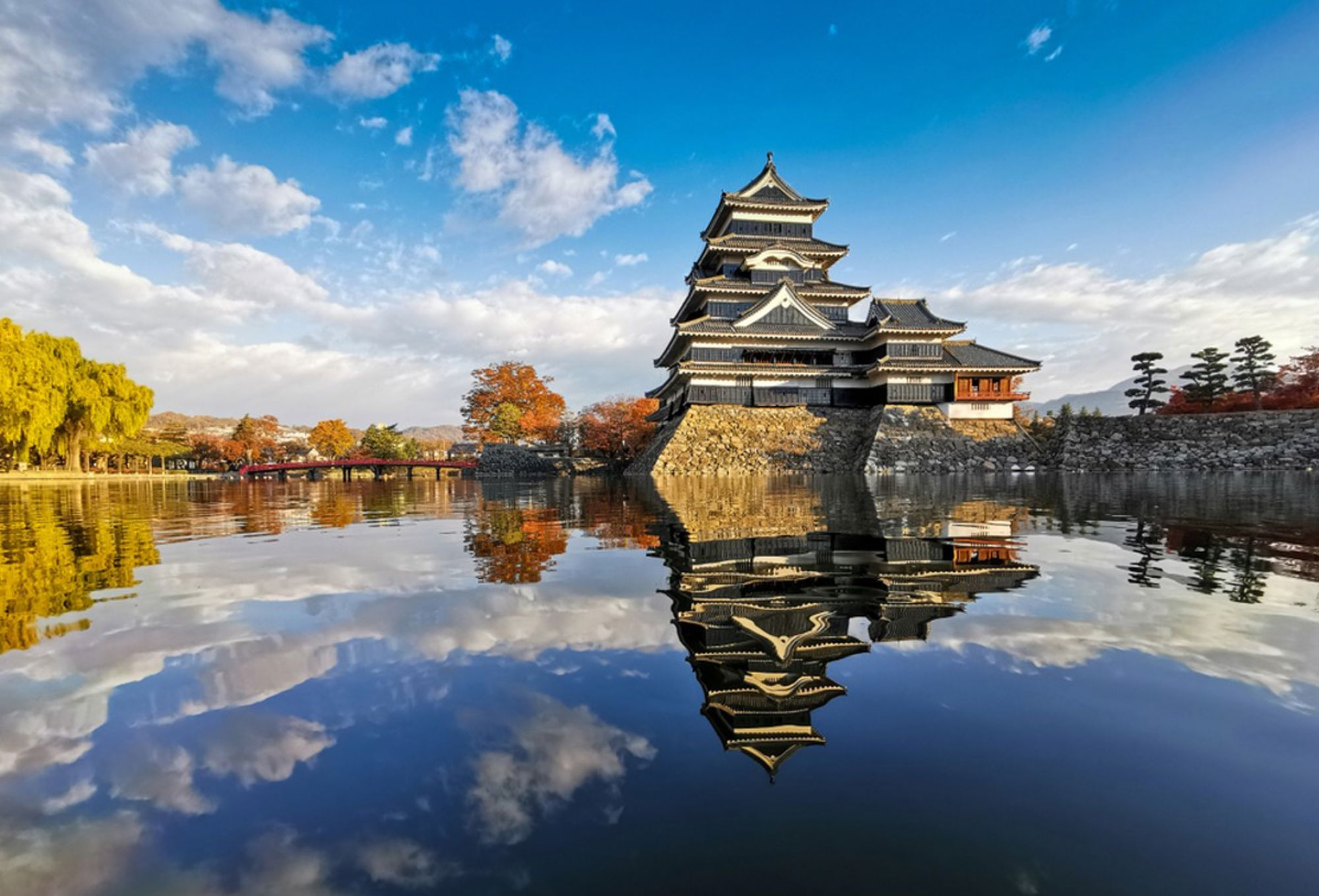 Matsumoto-kasteel in Japan weerspiegeld in de slotgracht onder een blauwe lucht.