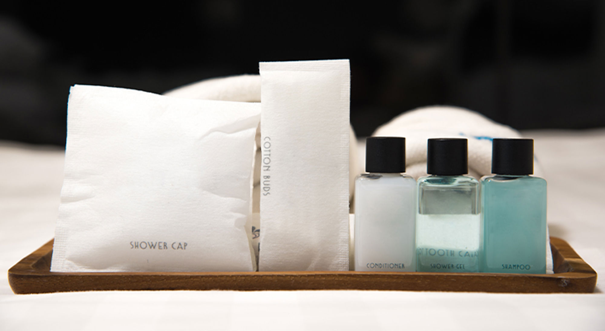 Toiletmini's hotel Hoteltoiletartikelen op een houten tray, met shampoo, conditioner, douchegel en douchekapje.