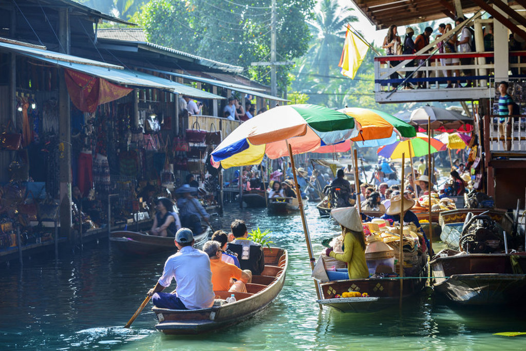 Drijvende markt in Thailand met kleurrijke parasols en boten vol koopwaar tijdens een groepsrondreis Thailand.