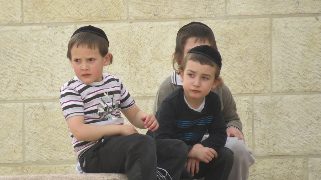 Twee jongens met keppeltje zitten op een stenen rand in Israël.