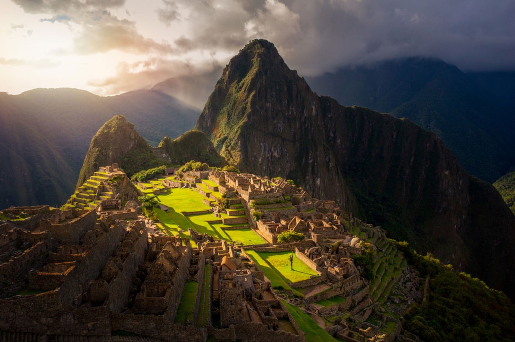 Machu Picchu in Peru met ruïnes en groene terrassen, omringd door bergen in avondlicht.