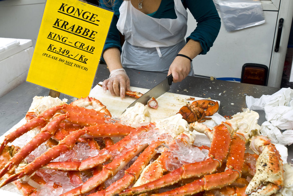 Verse koningkrab op ijs op een Scandinavische vismarkt, terwijl een verkoper de krab in stukken snijdt.