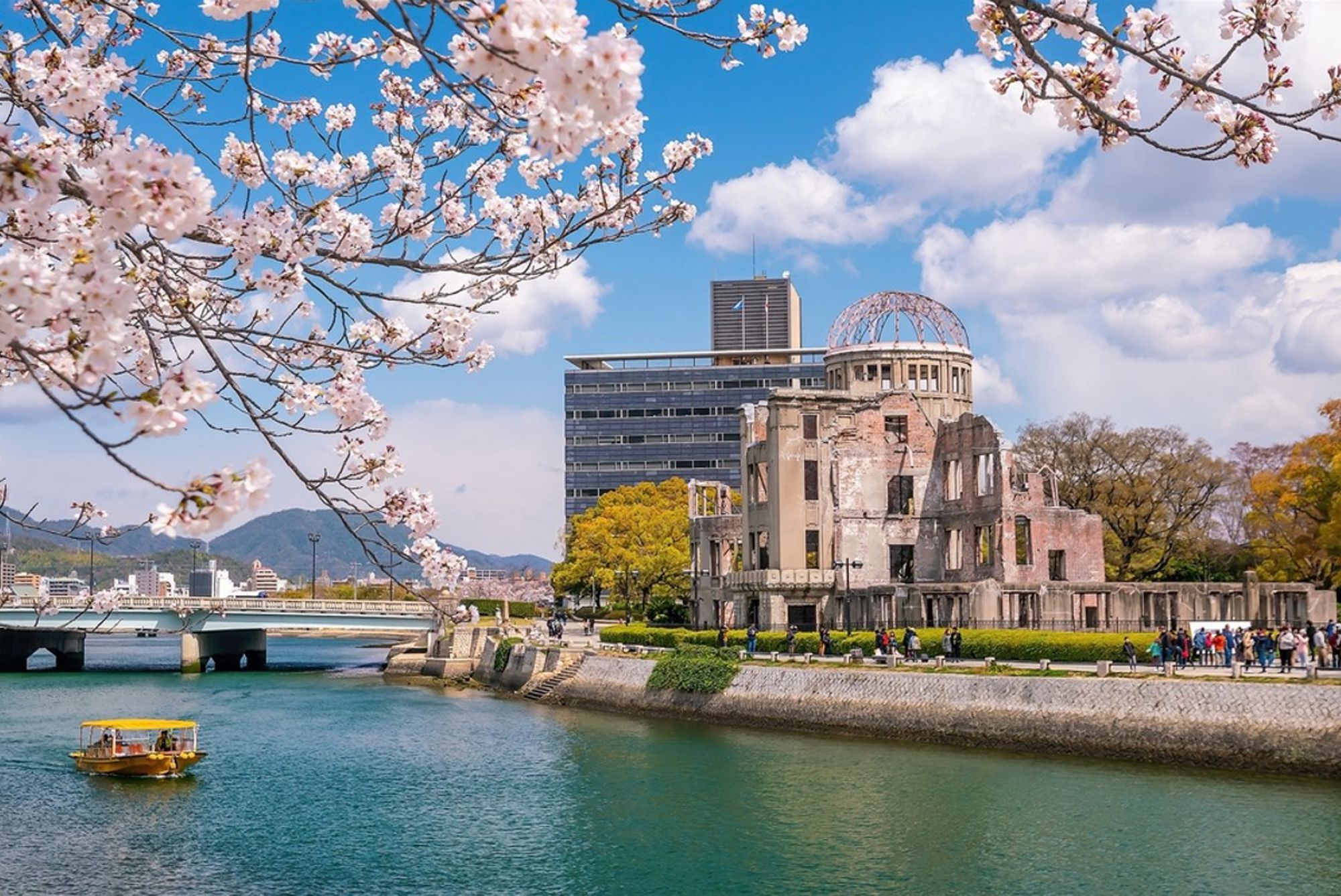 Kersenbloesem bij de Genbaku Dome in Hiroshima, met rivier en boot op de voorgrond.