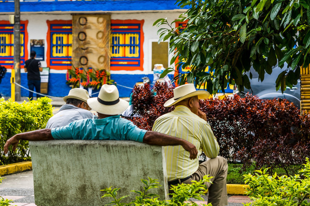 Mannen met hoeden op een bankje in een kleurrijk dorp in Colombia tijdens een groepsrondreis.