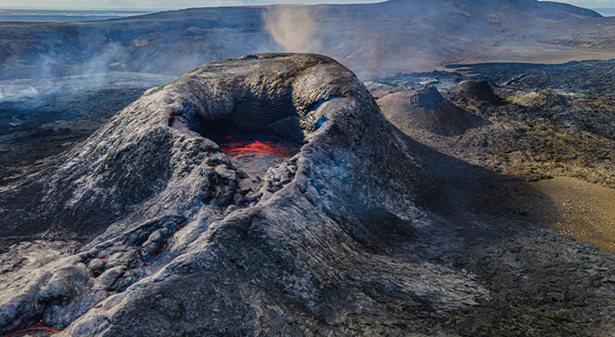 Actieve vulkaan IJsland Rokende vulkaan met gloeiende lava in de krater, omringd door ruig lavalandschap.