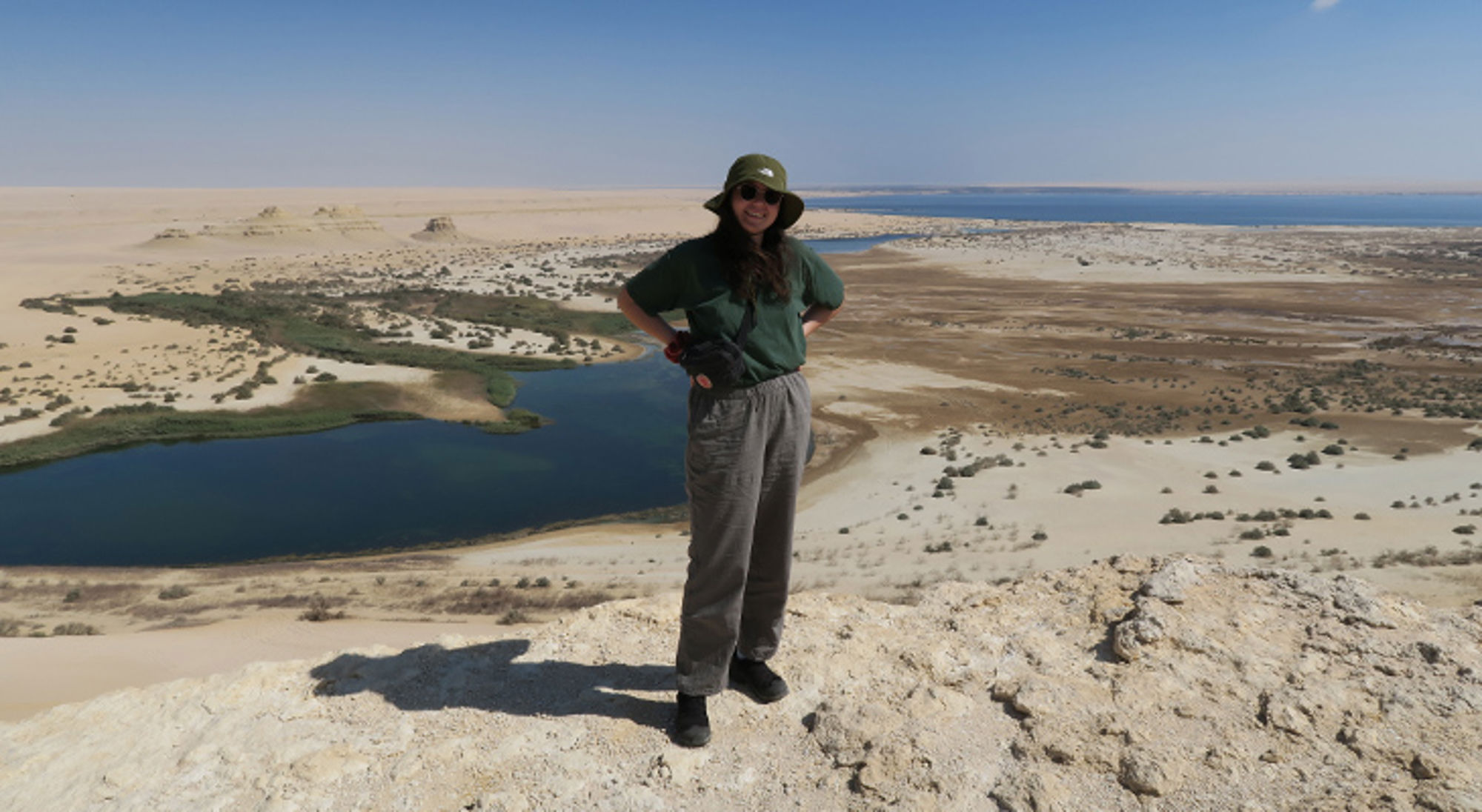 Britt in Egypte Reiziger op een duin met uitzicht op een blauwe lagune en uitgestrekte zandwoestijn.