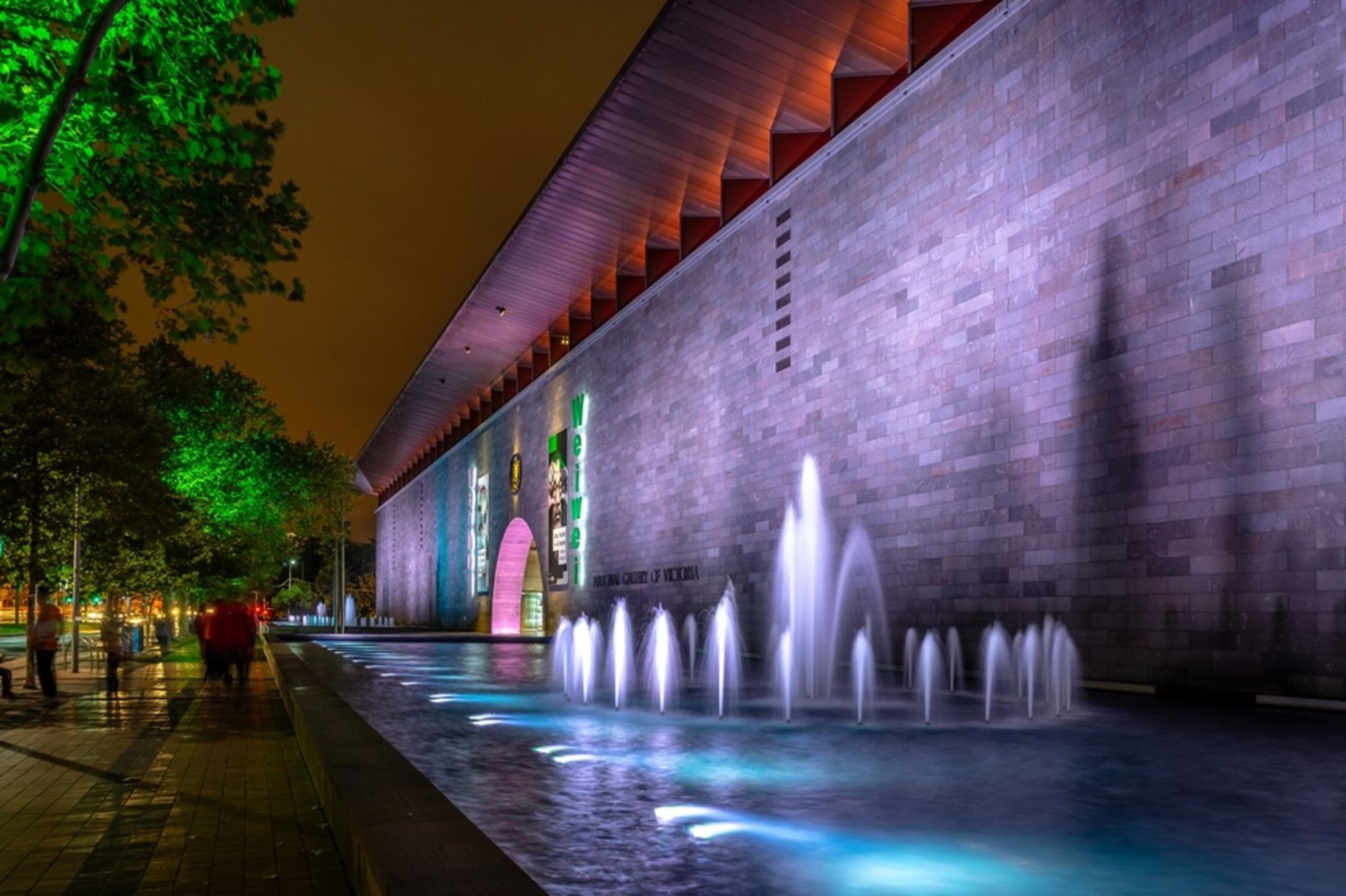 Night view of the National Gallery of Victoria in Melbourne with illuminated fountains in the foreground.