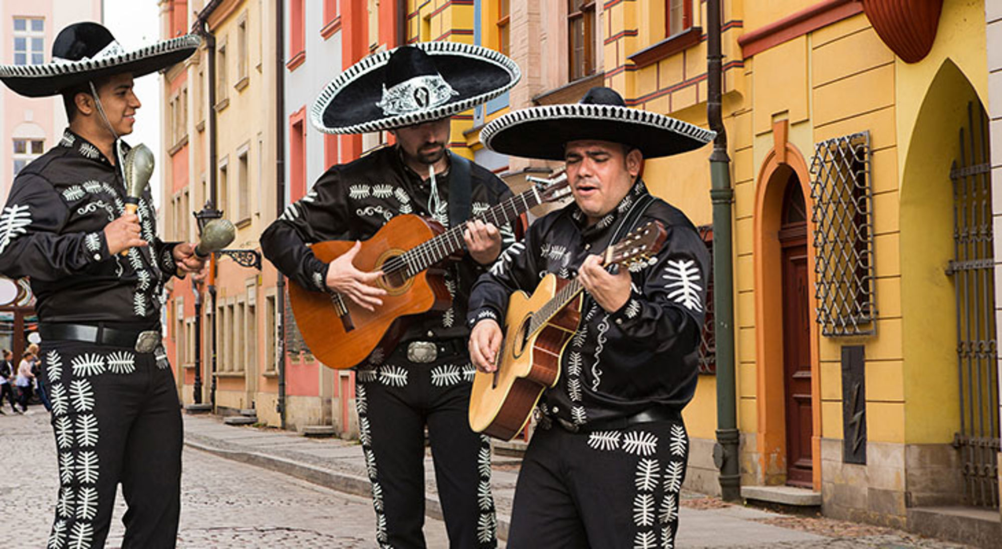 Mariachi-muzikanten spelen gitaar en maracas in een kleurrijke straat.