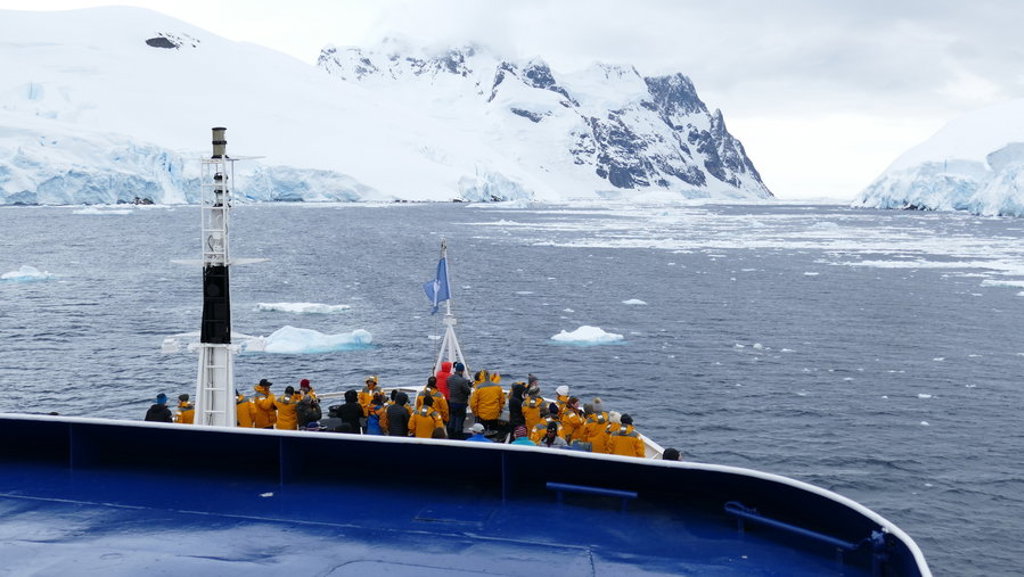 Passagiers op expeditieschip varen langs ijsbergen en besneeuwde bergen in Antarctica tijdens Crossing the Circle.