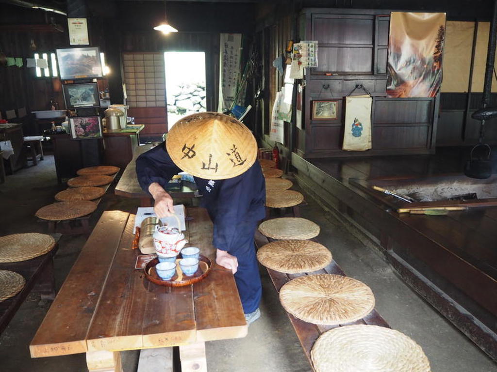 Japanse gastheer in traditioneel theehuis zet thee klaar op lage tafel met rieten kussens.