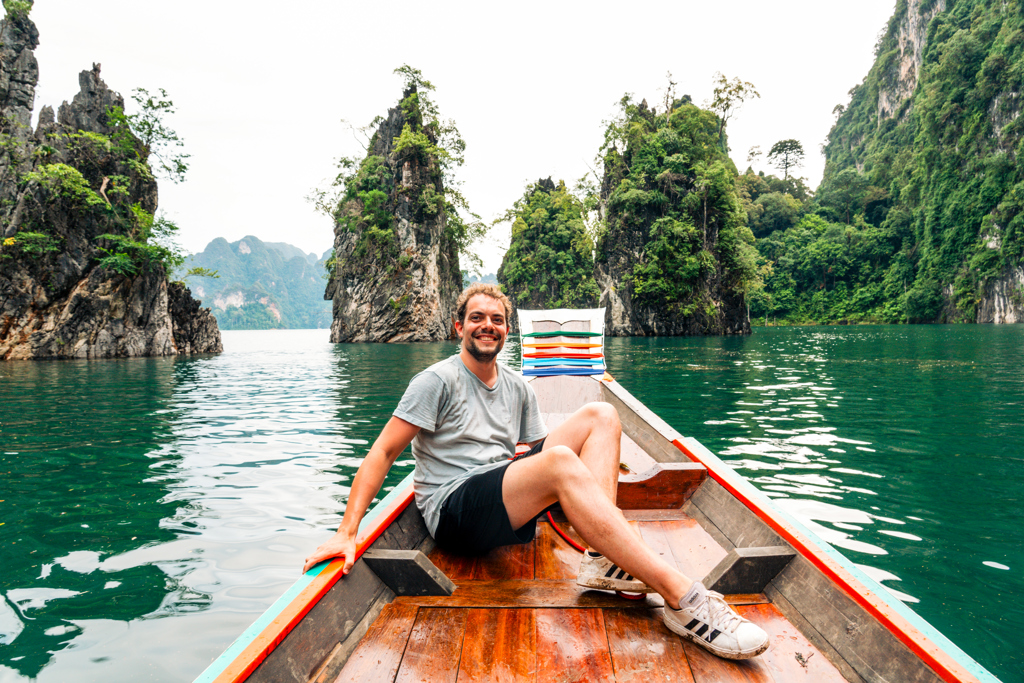 Man zit in een longtailboot op een groen meer tussen kalkstenen rotsen in Thailand tijdens een 22-35ers reis.