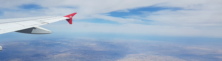 Vliegtuigvleugel boven wolken en landschap, symbool voor thuiskomen na een mooie reis.
