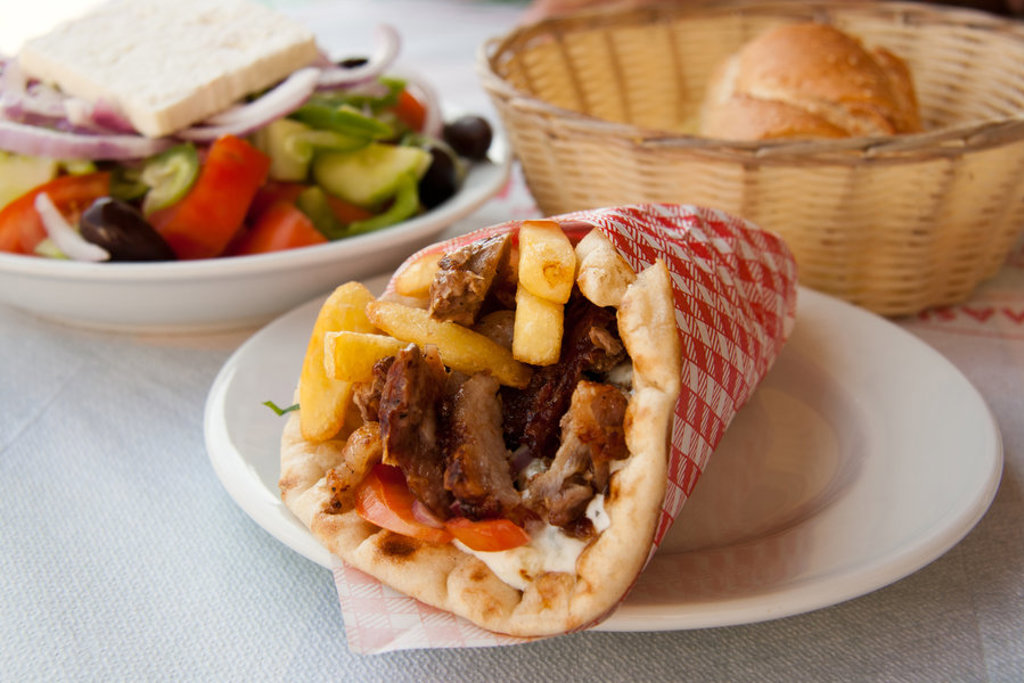 Griekse gyros in pita met friet, geserveerd met Griekse salade en broodmandje.