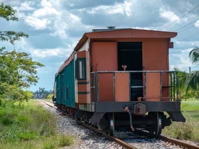 Achterzijde van een trein op het spoor in Cuba, omringd door groen landschap onder een bewolkte lucht.