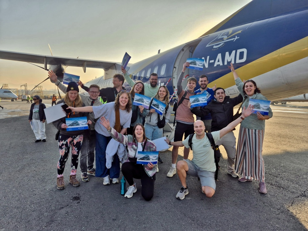 Groep 22-35ers reizigers poseert juichend op het vliegveld bij het vliegtuig, klaar voor de reis naar Nepal.